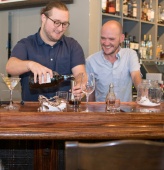 Two men prepare drinks behind a bar.