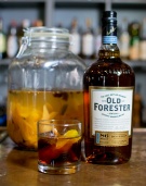 A Tumblr and bottle of Old Forester Kentucky Whisky sit on a bar.