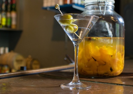 A martini class with two green olives sits on the bar.