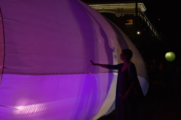 A girl with an outstretched arm, touches the lantern tent which is bathed in purple light.